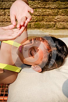 Southeast Asian ethnicity little girl lying down on a bench, sunbathing in the morning at home. hand rising up to cover her face