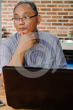 Southeast Asian Ethnicity mature adult man contemplating while working on a laptop at home. Thinking of continuation of his