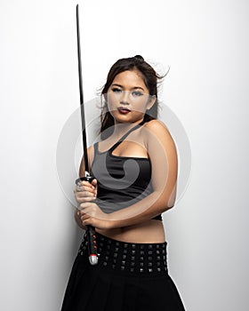 Southeast Asian girl in a black top and skirt with a sword against a white wall