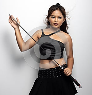 Southeast Asian girl in a black top and skirt with a sword against a white wall