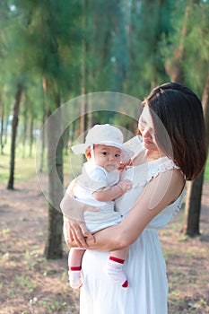 Southeast Asian mother and daughter wearing white dress. New born is 3 months old. Mom is holding her newborn.