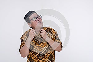 A southeast asian muslim man fanning his shirt while looking up feeling hot and comfortable. Wearing a batik shirt and songkok