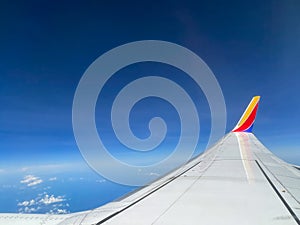 Southwest airplane wing flying above the clouds on a bright blue sky day