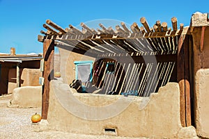 Southwestern US Adobe dwelling with pole ramada sunshade over patio and painted details in turquoise with pumpkins sitting around