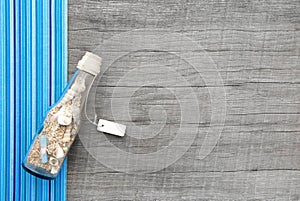 Souvenir bottle with sand and seashell on wooden background