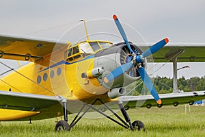 Soviet aircraft biplane Antonov AN-2 with yellow fuselage parked on a green grass of airfield closeup on a cloudy day