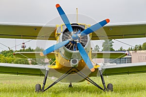 Soviet aircraft biplane Antonov AN-2 with blue four blade propeller and yellow fuselage parked on a green grass of airfield