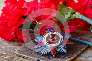 Soviet order of Patriotic War inscription Patriotic war with red carnations on an old wooden table. May 9 day of victory in the