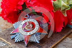 Soviet order of Patriotic War inscription Patriotic war with red carnations on an old wooden table. May 9 day of victory in the