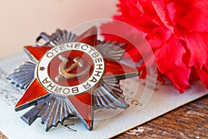 Soviet order of Patriotic war inscription Patriotic war with red carnations on an old wooden table. May 9 Victory day in the gre