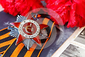 Soviet order of Patriotic war inscription Patriotic war with St. George`s ribbon and red carnations against the background of o