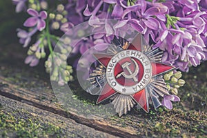 The Soviet order with Russian words Great Patriotic War, natural moss background with lilac branch, Victory Day 9 May