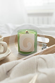 Soy candle and a cup of coffee on a tray. The tray is on a light white bed