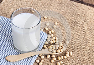 Soy milk in a glass with soybeans in spoon on sackcloth backgrou