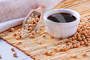 Soy sauce with soya beans scattered on a bamboo napkin against the background of burlap