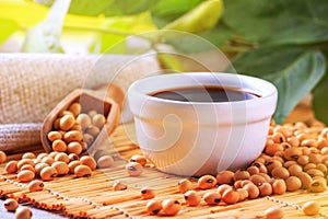 Soy sauce with soya beans scattered on a bamboo napkin against the background of burlap and branch young green pods soybean