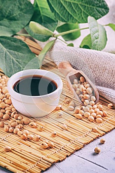Soy sauce with soya beans scattered on a bamboo napkin against the background of burlap and branch young green pods soybean