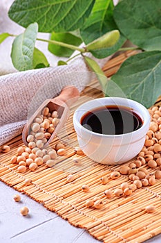 Soy sauce with soya beans scattered on a bamboo napkin against the background of burlap and branch young green pods soybean, close