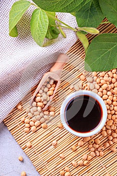 Soy sauce with soya beans scattered on a bamboo napkin against the background of burlap and branch young green pods soybean, top v