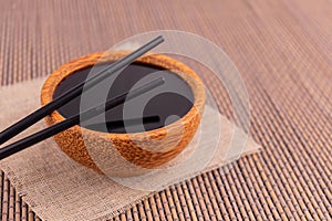 Soy sauce in a wooden bowl with chopsticks.