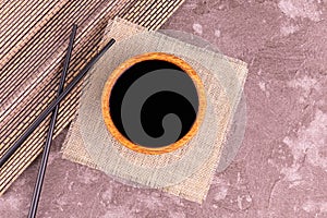 Soy sauce in a wooden bowl and chopsticks on a gray background.