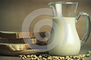 Soybean milk in a glass jug and whole wheat bread in wood disk on table.