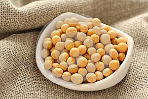 Soybeans in white ceramic bowl on sackcloth background photo