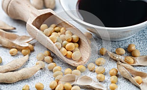 Soybeans in wooden spoon, pods and soy sauce in a white bowl