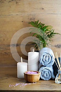 spa and aromatherapy concept-candles, towels, pink sea salt and an aromatic reed diffuser on a wooden table