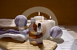 Spa aromatherapy still life with aroma oil bottle, purple bath bombs and lit candles.