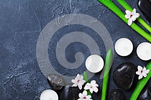 Spa background with massage pebble, green leaves, flowers and candles on black stone table from above. Aromatherapy, beauty.