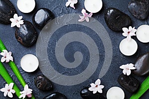 Spa background with massage pebble, green leaves, flowers and candles on black stone table top view. Aromatherapy, beauty.