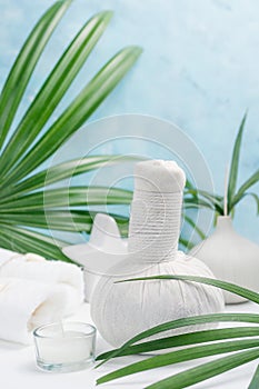 Spa background: thai massage bag, cosmetics, towels and palm leaves on blue background. Healthy lifestyle