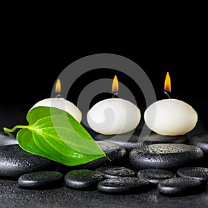 spa background of white candles and green leaf on black zen stones background with dew, closeup