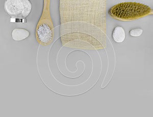 Spa bath massage treatment. Sea salt, natural brush and pebbles, tropical leaves on grey background.