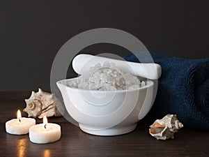 Spa composition with bowl filled with sea salt, towel, burning candles and sea shells. Concept of self care in bath or salon