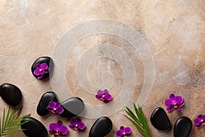 Spa composition with flowers, green leaves and massage stone on brown background top view. Beauty and relaxation. Flat lay