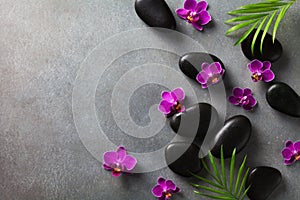 Spa composition with flowers, green leaves and massage stone on gray background top view. Beauty treatment and relaxation concept.