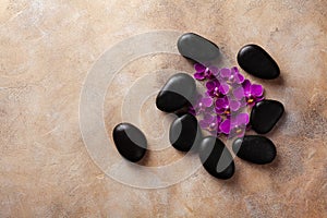 Spa composition with flowers and massage stone on brown background top view. Beauty treatment and relaxation concept. Flat lay