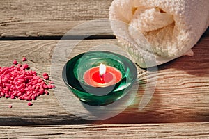 Spa composition with fresh rolled towel, lit candle and pink salt on a wooden background.