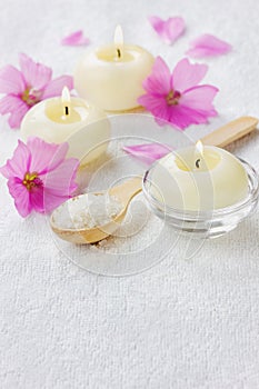 Spa composition with sea salt bath in wooden spoon, pink flowers and burning candles