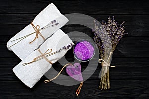 Spa concept. Lavender salt for a relaxing bath, handmade soap, white towels and dry lavender flowers on a black wooden background