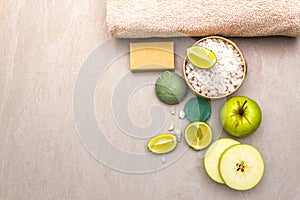 Spa concept, natural ingredients. Bath towel, sea salt with lime, apple, olive and mint soap, sponge. On a stone background, top