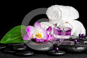 spa concept of orchid flower, zen basalt stones with drops, purple candles, beads and white towels, closeup