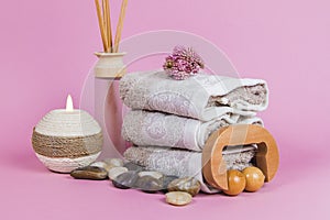 Spa essentials, aroma sticks stones, towels and a plant on a pink background