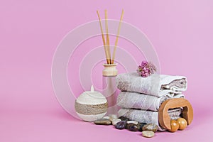 Spa essentials, aroma sticks stones, towels and a plant on a pink background