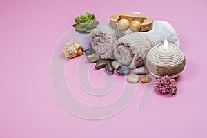 Spa essentials, aroma sticks stones, towels and a plant on a pink background