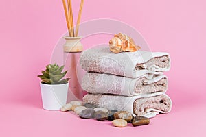 Spa essentials, aroma sticks stones, towels and a plant on a pink background  Keywords language: English