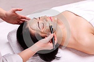 Spa facial mask application. Beautiful relaxed woman having clay face mask in the spa photo