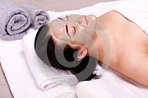 Spa facial mask application. Beautiful relaxed woman having clay face mask in the spa photo